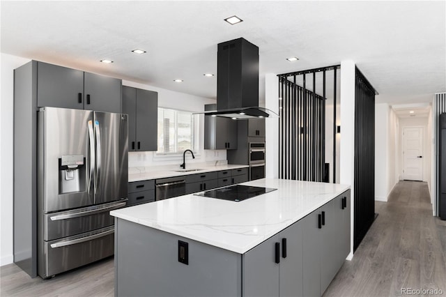 kitchen with island range hood, a center island, light stone countertops, stainless steel appliances, and a sink