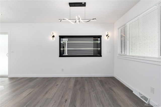 unfurnished room with a notable chandelier, dark wood finished floors, visible vents, and baseboards