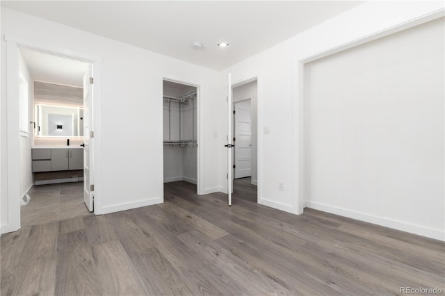 unfurnished bedroom with a spacious closet, ensuite bath, wood finished floors, and baseboards