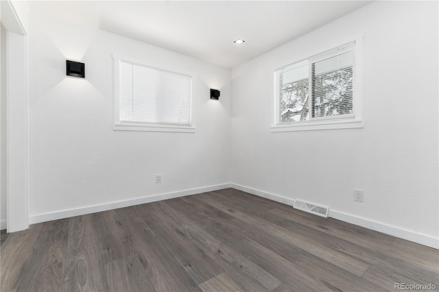 spare room with dark wood-type flooring, visible vents, and baseboards