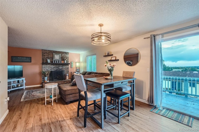 dining space featuring a textured ceiling, a notable chandelier, hardwood / wood-style flooring, and a fireplace