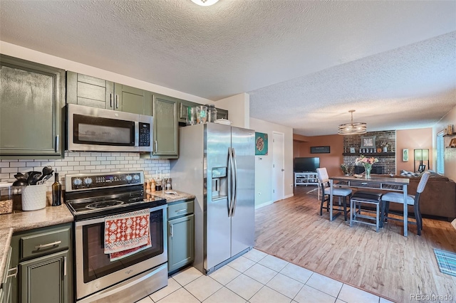 kitchen with green cabinetry, light tile patterned flooring, decorative backsplash, pendant lighting, and appliances with stainless steel finishes