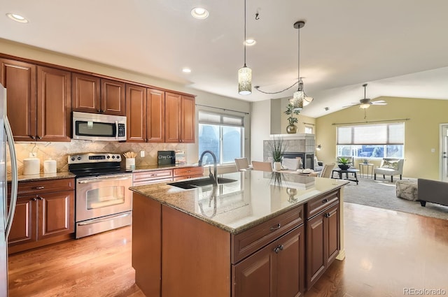 kitchen with stainless steel appliances, lofted ceiling, sink, a kitchen island with sink, and a fireplace