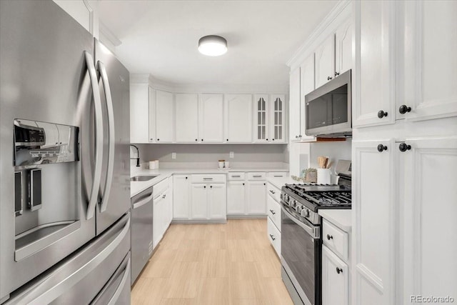 kitchen featuring glass insert cabinets, light countertops, appliances with stainless steel finishes, white cabinets, and a sink