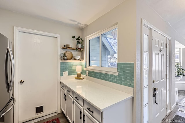 kitchen with white cabinets, freestanding refrigerator, light countertops, open shelves, and backsplash