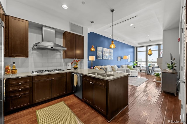 kitchen featuring wall chimney exhaust hood, stainless steel appliances, pendant lighting, sink, and kitchen peninsula