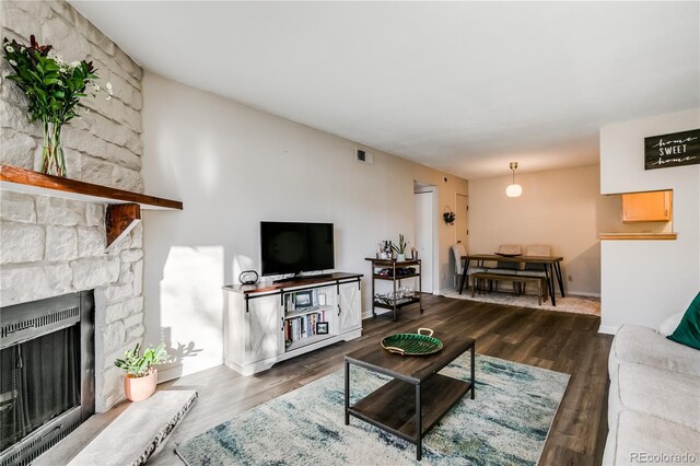 living room featuring a stone fireplace, dark wood-type flooring, visible vents, and heating unit