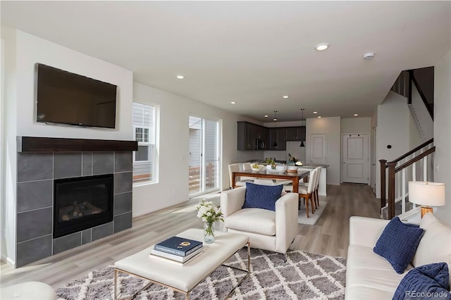 living room featuring light wood-style floors, recessed lighting, stairway, and a tiled fireplace