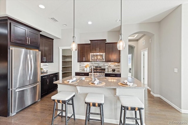 kitchen featuring decorative light fixtures, a kitchen island with sink, stainless steel appliances, and hardwood / wood-style flooring