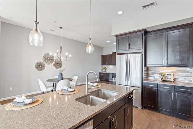 kitchen with stainless steel fridge, dark brown cabinetry, light hardwood / wood-style flooring, sink, and light stone countertops