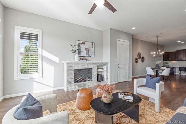 living room featuring wood-type flooring, ceiling fan with notable chandelier, and a stone fireplace