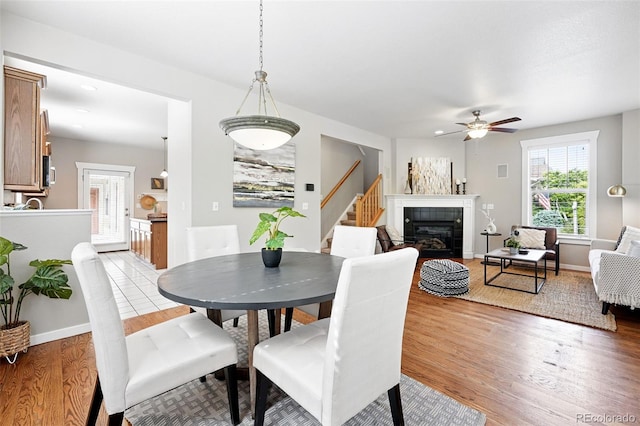 9134 E 29th Pl, Denver, CO 80238 - dining area with light wood-type flooring, stairway, a ceiling fan, a tiled fireplace, and baseboards