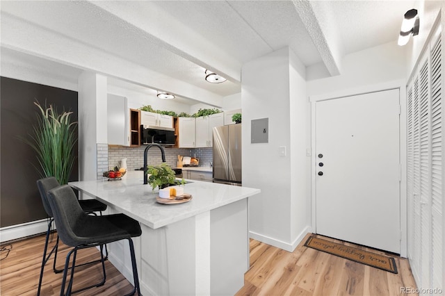 kitchen with a breakfast bar, white cabinetry, light hardwood / wood-style flooring, appliances with stainless steel finishes, and kitchen peninsula