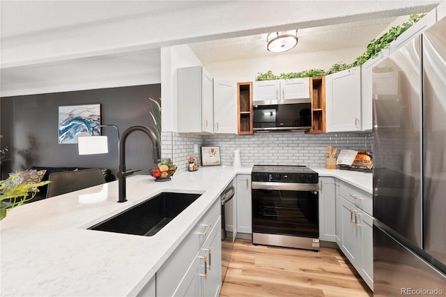 kitchen with appliances with stainless steel finishes, tasteful backsplash, sink, light hardwood / wood-style floors, and light stone countertops