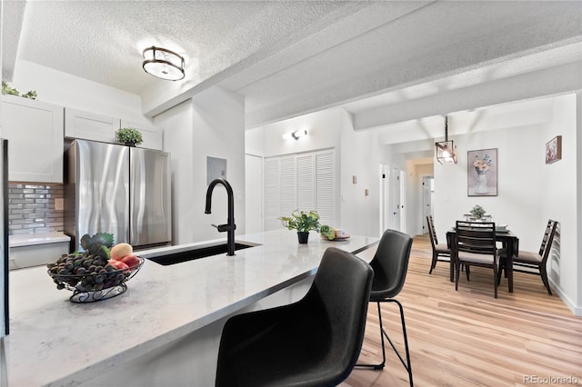 kitchen with decorative light fixtures, sink, stainless steel fridge, a kitchen breakfast bar, and light hardwood / wood-style flooring