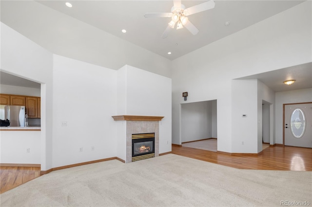 34771 E 153rd Ct, Hudson, CO 80642 - unfurnished living room featuring a towering ceiling, light colored carpet, a ceiling fan, a tile fireplace, and light wood finished floors