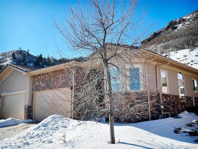 view of snowy exterior with a garage and a mountain view