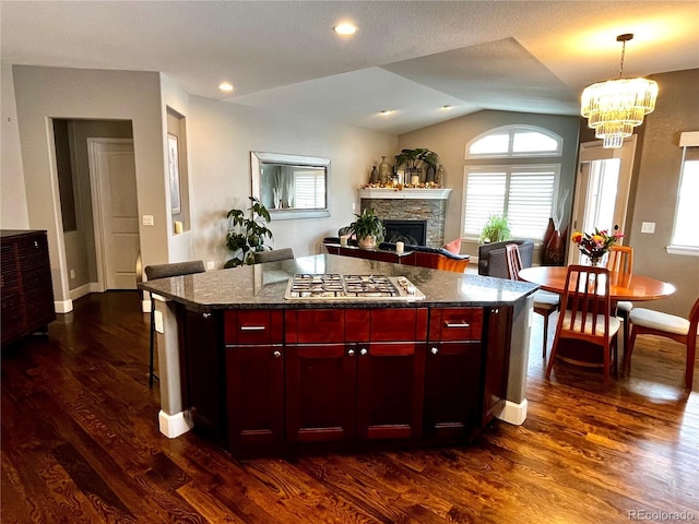 kitchen featuring vaulted ceiling, a kitchen island, a stone fireplace, stainless steel gas stovetop, and dark hardwood / wood-style flooring