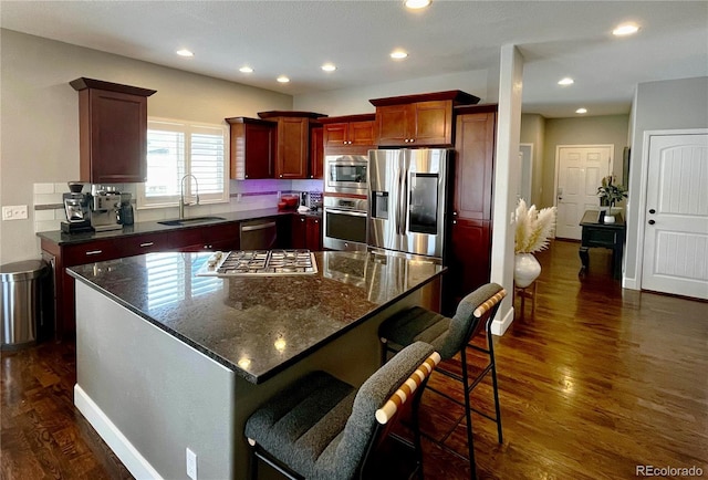 kitchen with a kitchen island, appliances with stainless steel finishes, sink, dark stone countertops, and dark hardwood / wood-style flooring