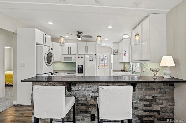 825 Hill Road Ct, Colorado Springs, CO 80909 - kitchen featuring refrigerator with ice dispenser, estacked washer and dryer, white microwave, dark wood finished floors, and a peninsula