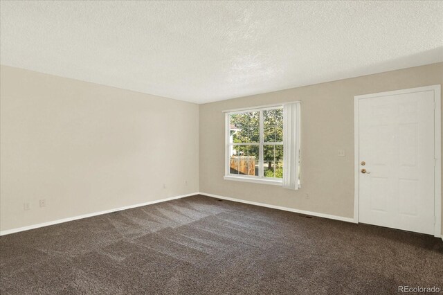 spare room featuring dark colored carpet and a textured ceiling