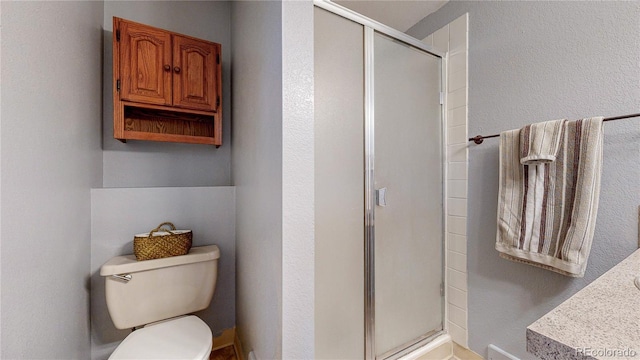 bathroom featuring a stall shower, toilet, and a textured wall