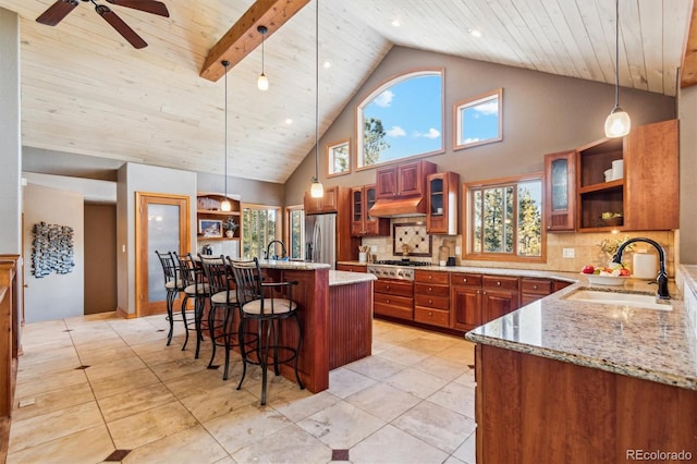 kitchen featuring pendant lighting, sink, stainless steel appliances, light stone countertops, and a center island with sink