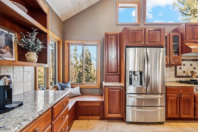 kitchen featuring vaulted ceiling, plenty of natural light, stainless steel fridge, and light stone counters