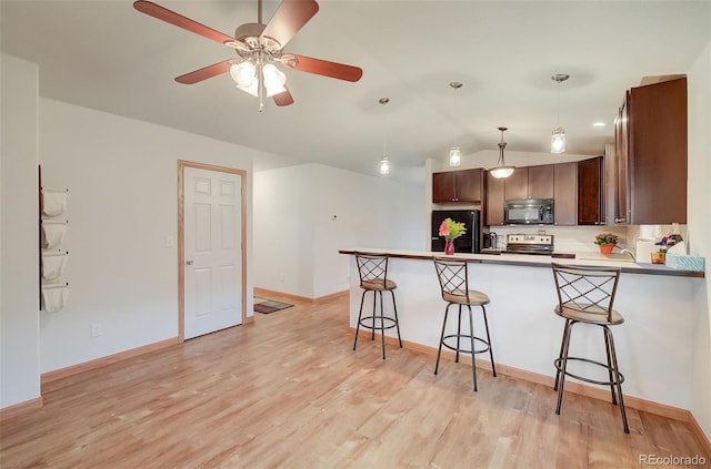 kitchen featuring a kitchen bar, black appliances, light wood-style floors, a peninsula, and vaulted ceiling