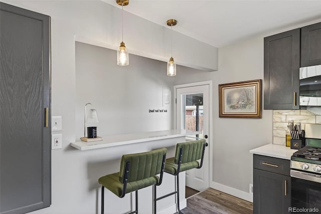 2050 S Wolff St, Denver, CO 80219 - kitchen featuring appliances with stainless steel finishes, dark wood-style floors, tasteful backsplash, light countertops, and a kitchen breakfast bar