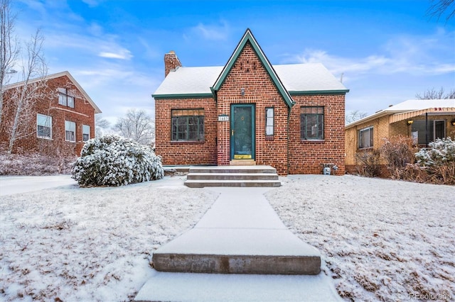 english style home featuring a chimney and brick siding