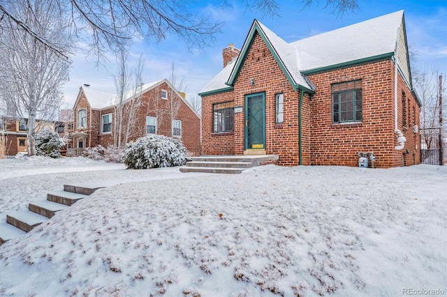 tudor-style house featuring a chimney and brick siding