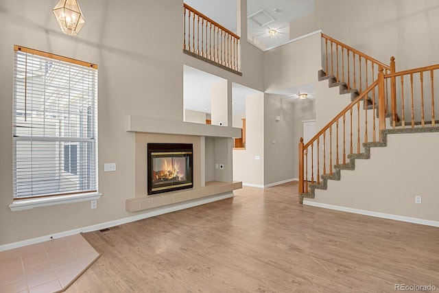 9874 Grove St Unit B, Westminster, CO 80031 - unfurnished living room with wood finished floors, healthy amount of natural light, stairs, a tiled fireplace, and a towering ceiling