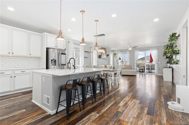 kitchen with a breakfast bar, hanging light fixtures, a center island with sink, stainless steel fridge, and white cabinets