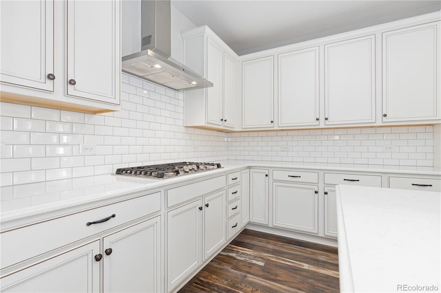 kitchen featuring wall chimney exhaust hood, stainless steel gas cooktop, dark hardwood / wood-style floors, white cabinets, and backsplash