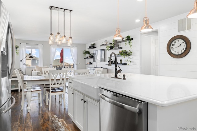 kitchen featuring pendant lighting, appliances with stainless steel finishes, white cabinetry, an island with sink, and dark hardwood / wood-style flooring