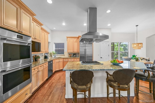 kitchen with appliances with stainless steel finishes, island exhaust hood, a sink, decorative backsplash, and a breakfast bar
