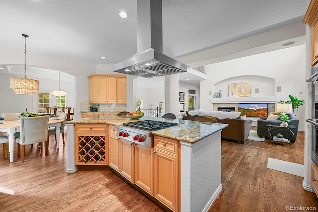 kitchen featuring appliances with stainless steel finishes, a fireplace, island exhaust hood, light wood-type flooring, and a chandelier