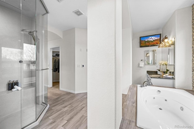 full bathroom featuring a stall shower, wood finished floors, a whirlpool tub, a spacious closet, and baseboards