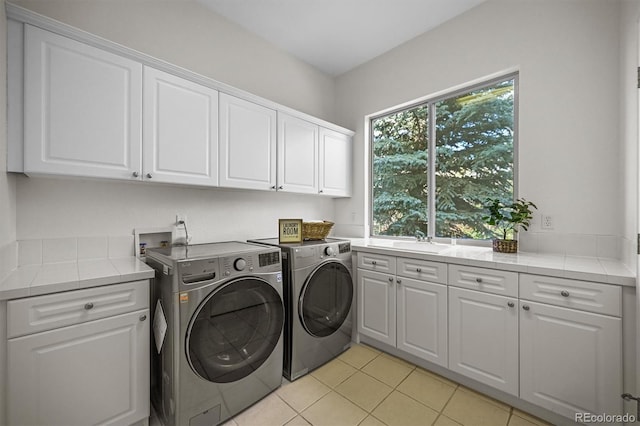 clothes washing area with cabinet space, washer and dryer, and light tile patterned floors