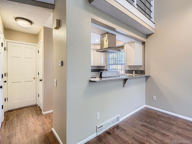 1990 S Helena St Unit H, Aurora, CO 80013 - kitchen featuring island exhaust hood, wood finished floors, white cabinetry, tasteful backsplash, and a breakfast bar