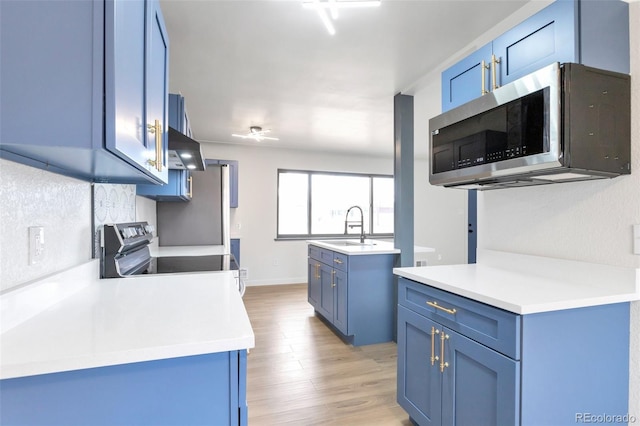 kitchen featuring blue cabinetry, exhaust hood, sink, and stainless steel appliances