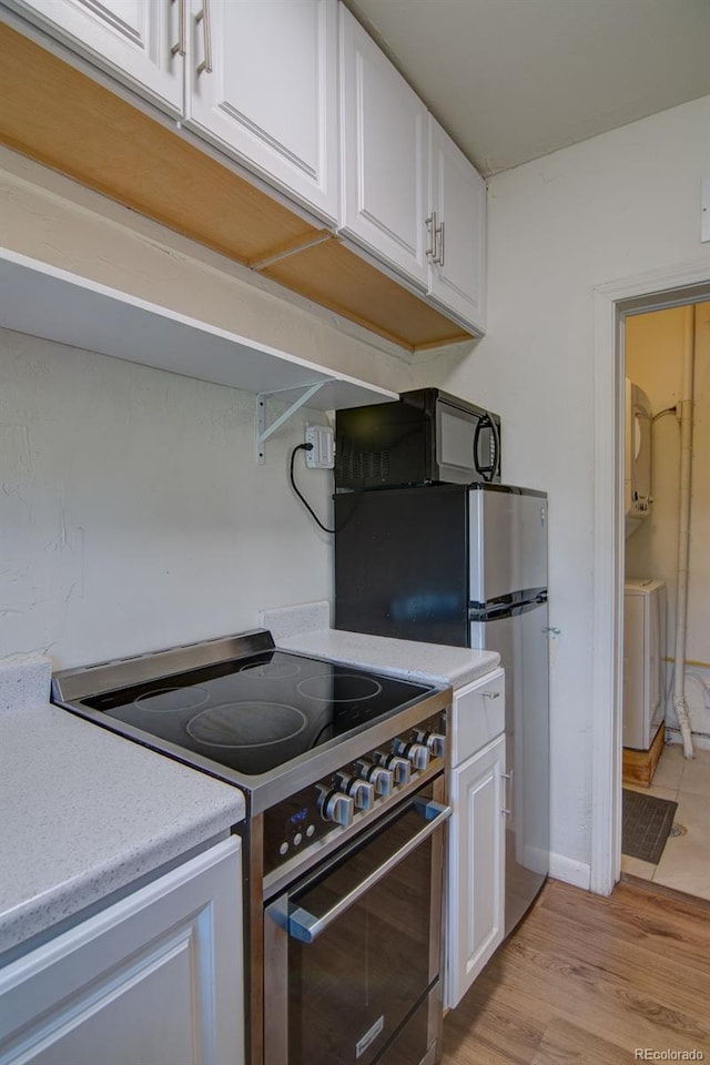 1560 Simms St, Lakewood, CO 80215 - kitchen with electric range, washer / dryer, white cabinets, light countertops, and black microwave