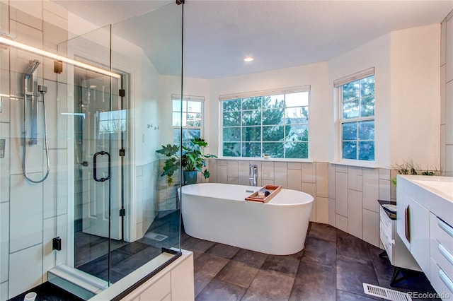 bathroom featuring plus walk in shower, vanity, and tile walls