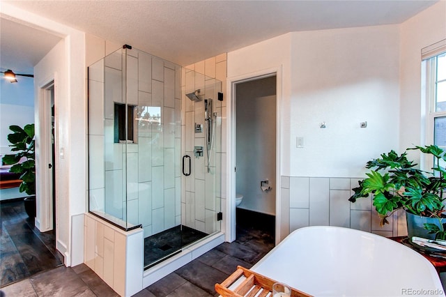 bathroom with a textured ceiling, hardwood / wood-style floors, shower with separate bathtub, and toilet