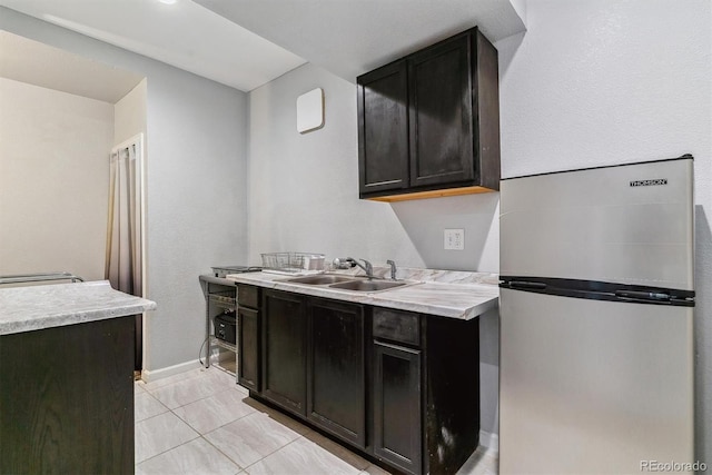 kitchen with freestanding refrigerator, light countertops, a sink, and light tile patterned floors