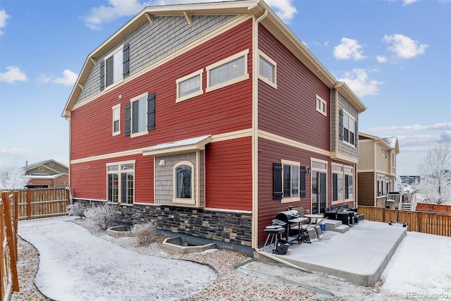 snow covered house featuring stone siding and fence