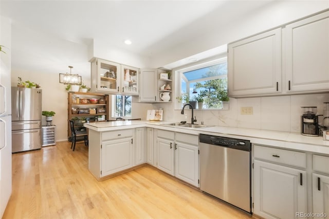 kitchen featuring stainless steel appliances, a sink, a peninsula, light countertops, and light wood finished floors