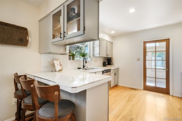 kitchen with a kitchen bar, a peninsula, a sink, glass insert cabinets, and light countertops