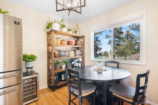 dining room with light wood-style flooring, a chandelier, wine cooler, and baseboards